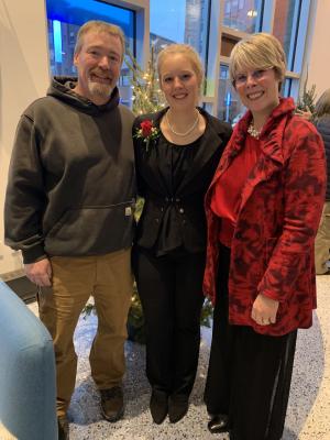 student stands smiling between her parents at a concernt.