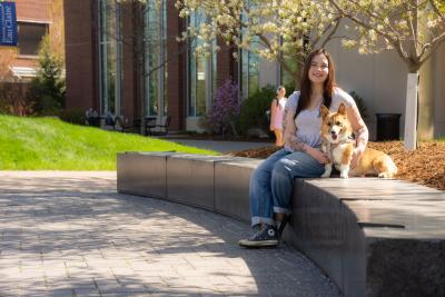 student and service dog seated on campus mall area on a sunny spring day 