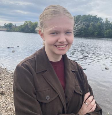 A close-up of UWEC student Elva Crist in front of a body of water with trees in the background
