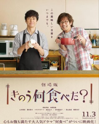 Two men in a kitchen cooking and smiling at the camera.