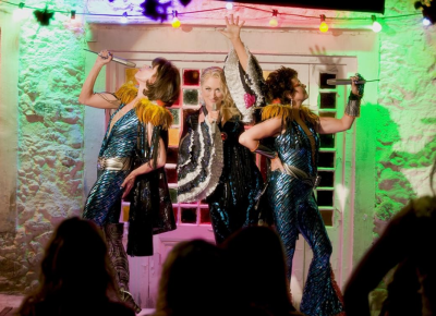 Three women singing in a local establishment with flashy outfits