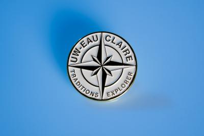 UW-Eau Claire Traditions Keeper coin. The coin is white with a compass arrow in the middle.