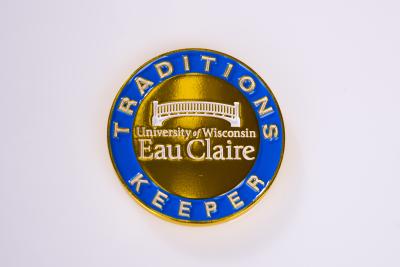 Traditions Keeper medallion. The medallion with navy blue and gold. The middle of the medallion has an image of the footbridge with UW-Eau Claire written below.
