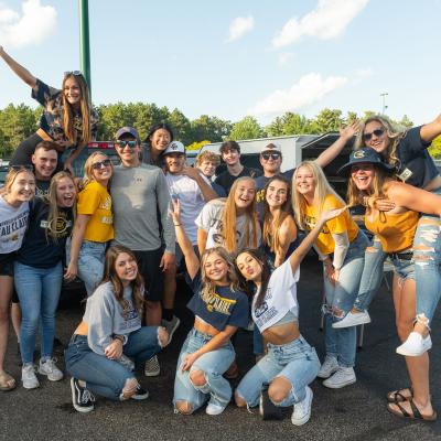 A large group of young people in blue and gold clothing pose and smile in a parking lot.