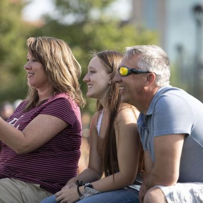 student and family sitting on a campus mall rock at an event, smiling
