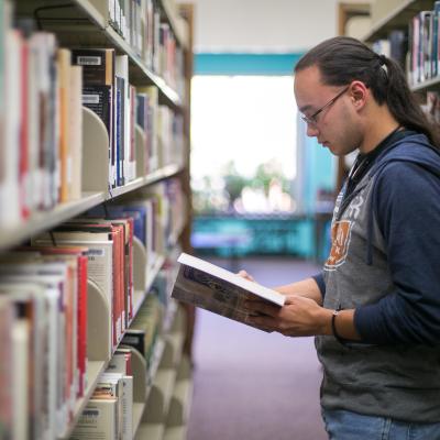 Male student in the library stacks looking at a book