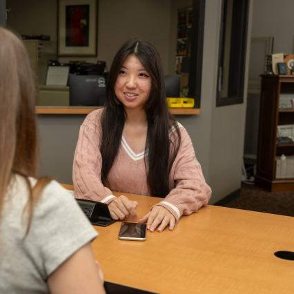 Student smiles at another student while sitting across from one another