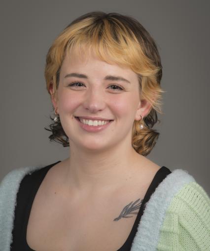 A headshot of Lauren. They are wearing a black top underneath a cardigan, their naturally brunette short hair is bleached blonde around the face.