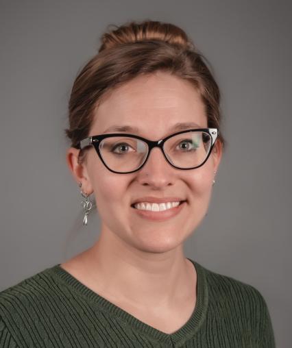 A headshot photo of Jenna wearing glasses and a v neck sweater
