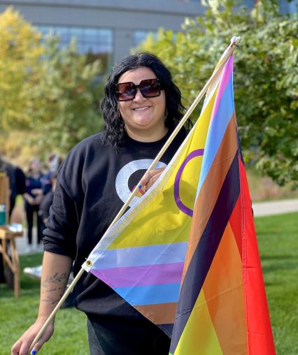 Women with short black hair holding progressive pride flag 