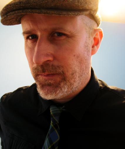 Image of Ned Gannon in a Tweed Hat and Plaid Tie.