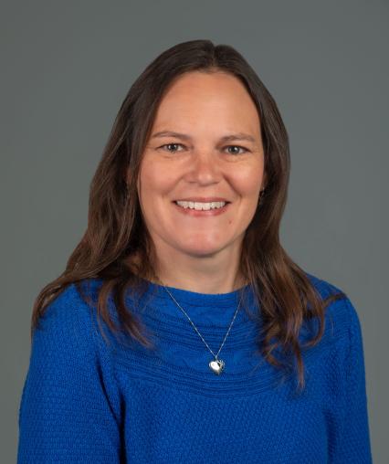 Picture of brown haired individual with blue sweater on a gray background
