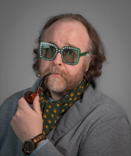 A very handsome gentlemen poses eloquently with a meerschaum pipe and rhinestone glasses on. He is a goofball.