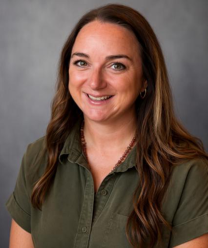 Headshot of Katelyn Leggio with long brown hair in a green short sleeved dress.