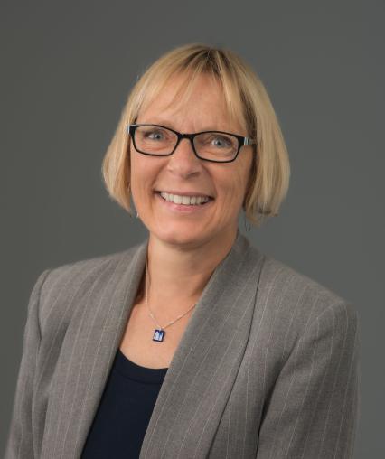 Headshot of woman with blue glasses and gray blazer.