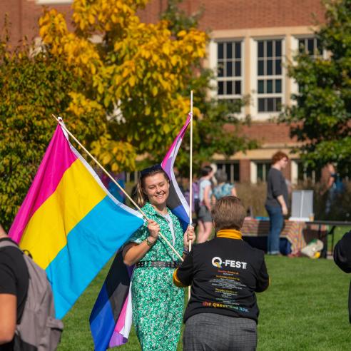 student with two PRIDE flags at outdoor event on campus mall