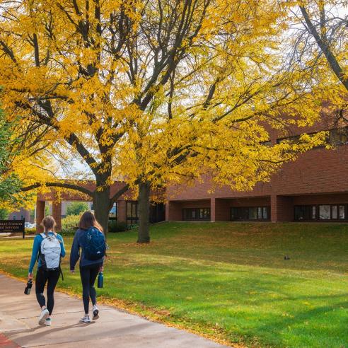 A picture showing student walking in front of the Human Science and Service hall surrounded by trees