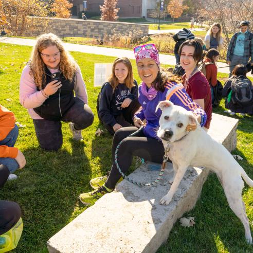 A group of students sitting on the grass and engaging with a friendly dog during the Bark Break event, enjoying a sunny day on campus.