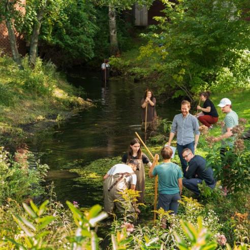 A group of people engaged in outdoor activities by a Phillips science hall small stream