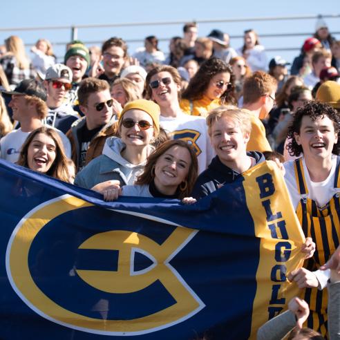  A group of cheerful students, holding a UWEC flag, enjoys a sunny day at a sports event, embodying school spirit and camaraderie.