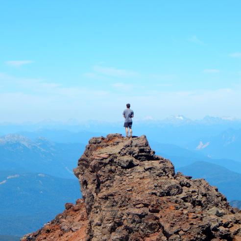 A student on a study abroad program in Chile, Valparaiso, standing on top of the rocky peak with an amazing scenario of blue sky and mountains