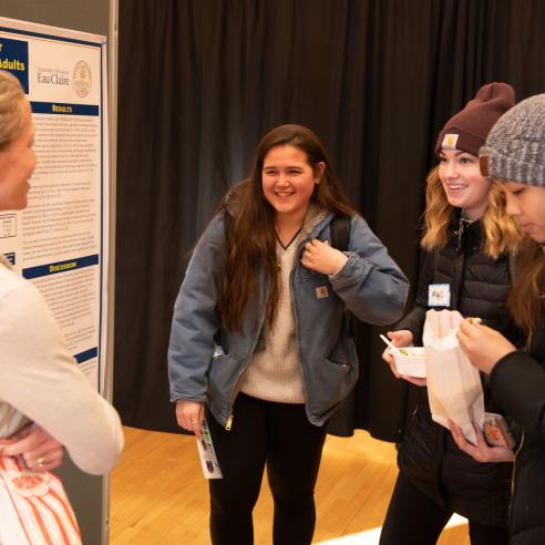 A group of students engaged in conversation at a university research presentation.