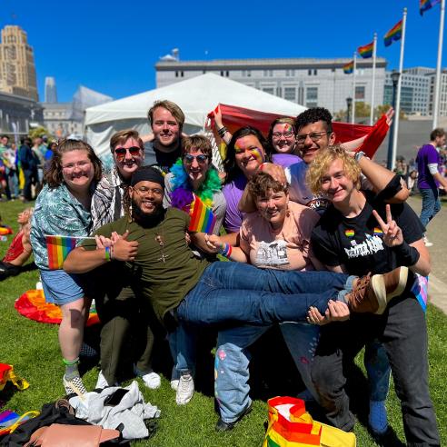 A group of students posing together at a Pride festival, sporting rainbow flags and vibrant attire