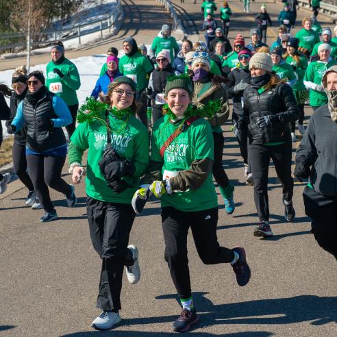 A group participants in a Shamrock Shuffle fundraiser dressed in festive green shirts and accessories showcasing community spirit
