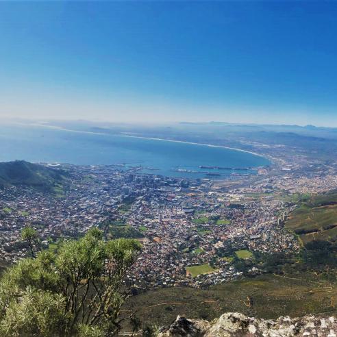 A view from Table Mountain in South Africa, overlooking Cape Town and its surrounding landscape, with the cityscape stretching towards the horizon and the ocean in the background.