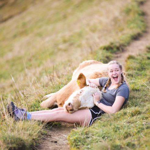 A student during study aboard in Sweden lying in the grass cuddling a cow