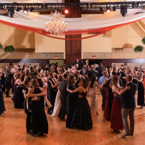 A grand ballroom filled with students elegantly dancing under a decorative chandelier at VBall event