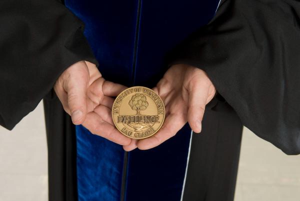 Faculty in regalia holding the Excellence Award medallion