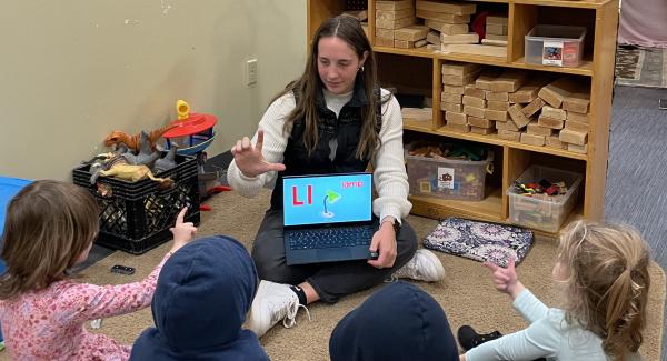 student teaching doing Americal Sign Language with youngsters, all seated on the floor