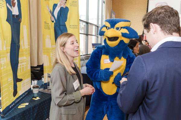School mascot talking with an employer at the career fair table.