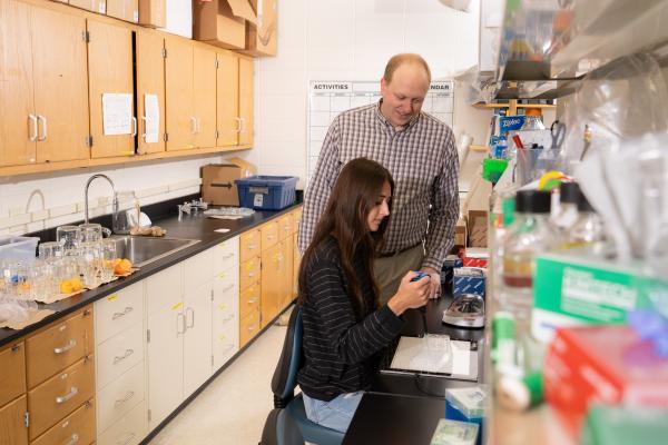 faculty person standing next to a seated student working in a chemistry lab 