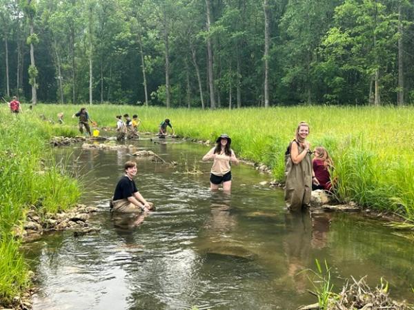 Students wade in a creek and smile while collecting water samples