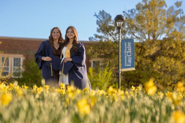 two grads in cap and gown in a flower bed 