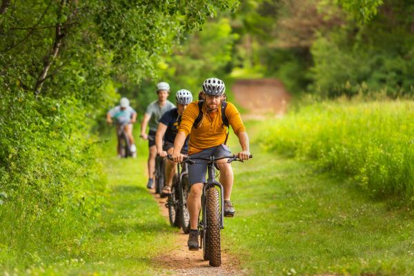 A group of bikers ride through a grassy trail in the summer