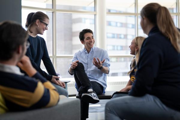 A group of students gather around a Business study space laughing and collaborating.
