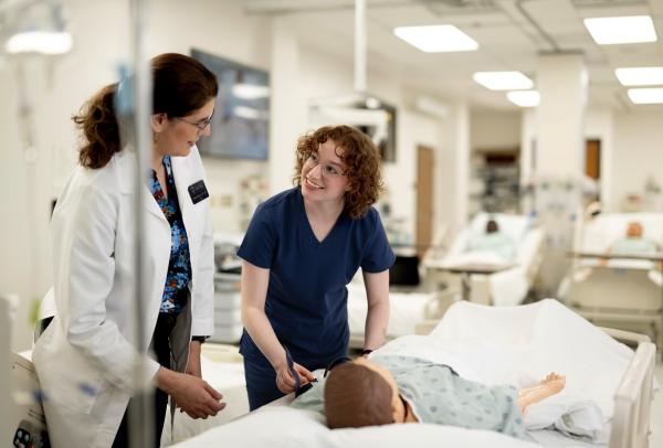 A Nursing student and professor work together over a manequin.