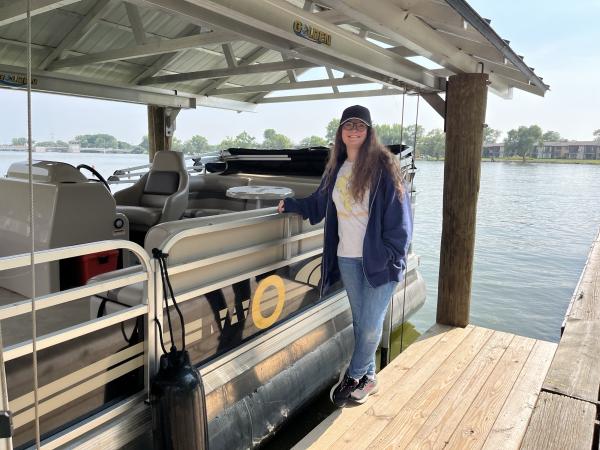student by a pontoon boat on waterfront dock 