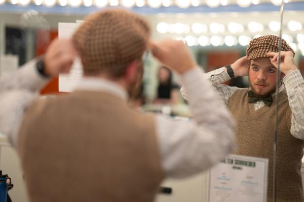 student checking hat in mirror backstage 