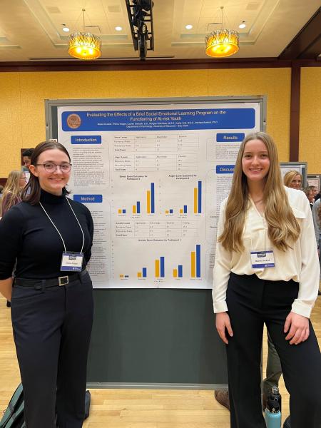 Students stand left and right of a research poster in a large presentation hall