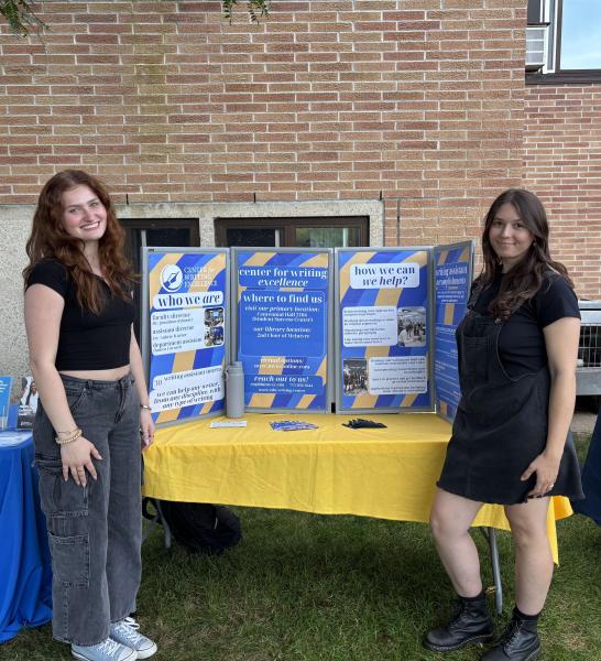 Bree Muske stands next to her peer in front of a Center for Writing Excellence informational poster