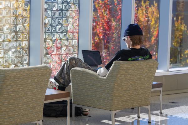 a sole student sitting in the sunny windows of Centennial, fall leaves outside