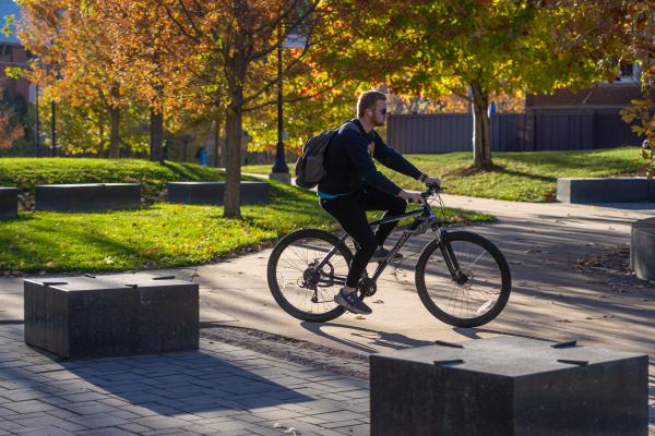 student on bike crossing campus, fall leaves 
