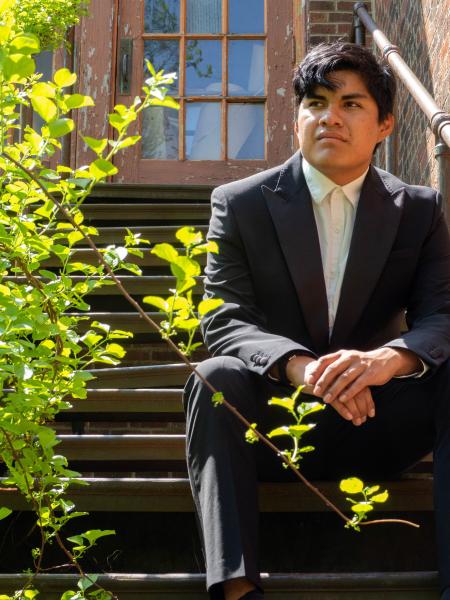 Honors student Kevin Miro in formal attire sitting on outdoor steps