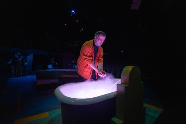 On stage, man with hand in tub topped with dry ice smoke 