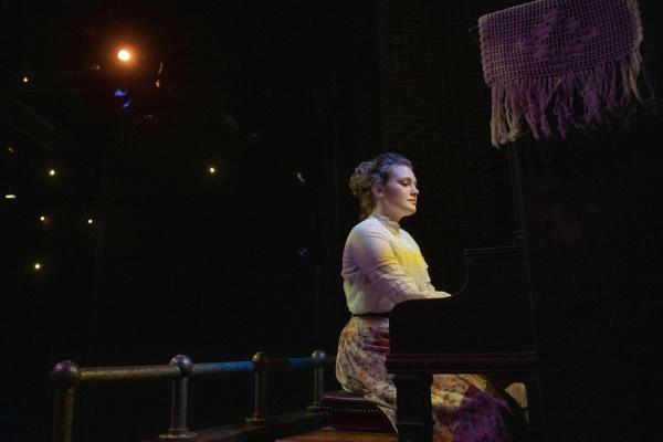 Female student at the piano on stage in early 1900's costume