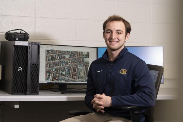 Male student smiling in a computer lab, sitting at a work station